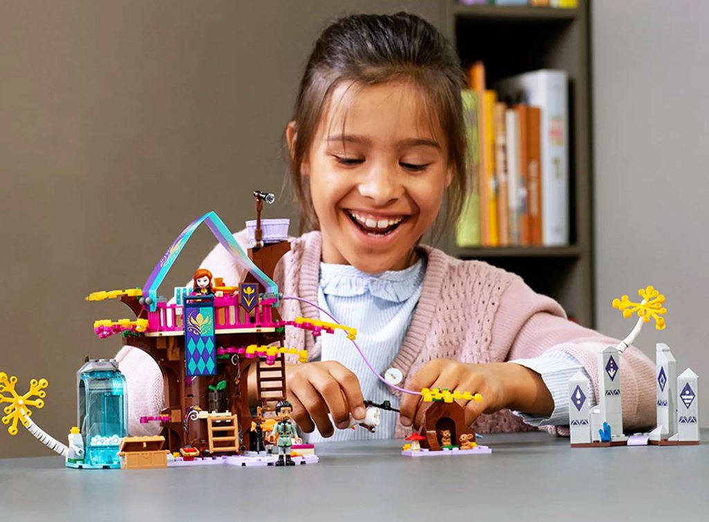 girl with black hair play with lego disney frozen treehouse set on a grey table