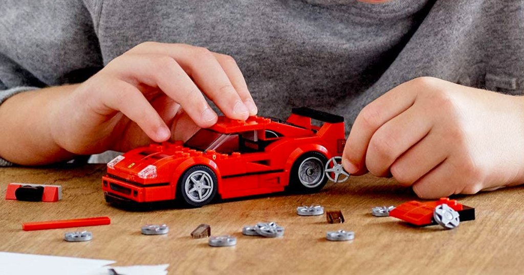 boy in grey shirt building a red lego ferrari car on a wood table