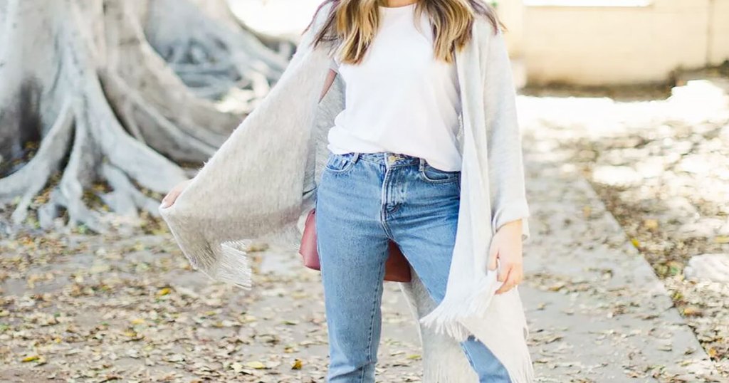 woman standing outside wearing white tee and jeans with a white wrap flowing in the wind