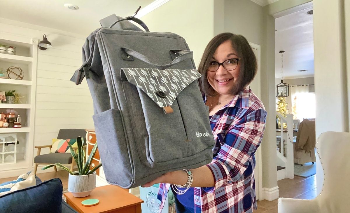 A woman holding a backpack up and smiling