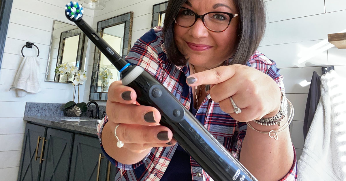 woman with short black hair in a plaid shirt holding up and pointing at a black oral-b electric toothbrush