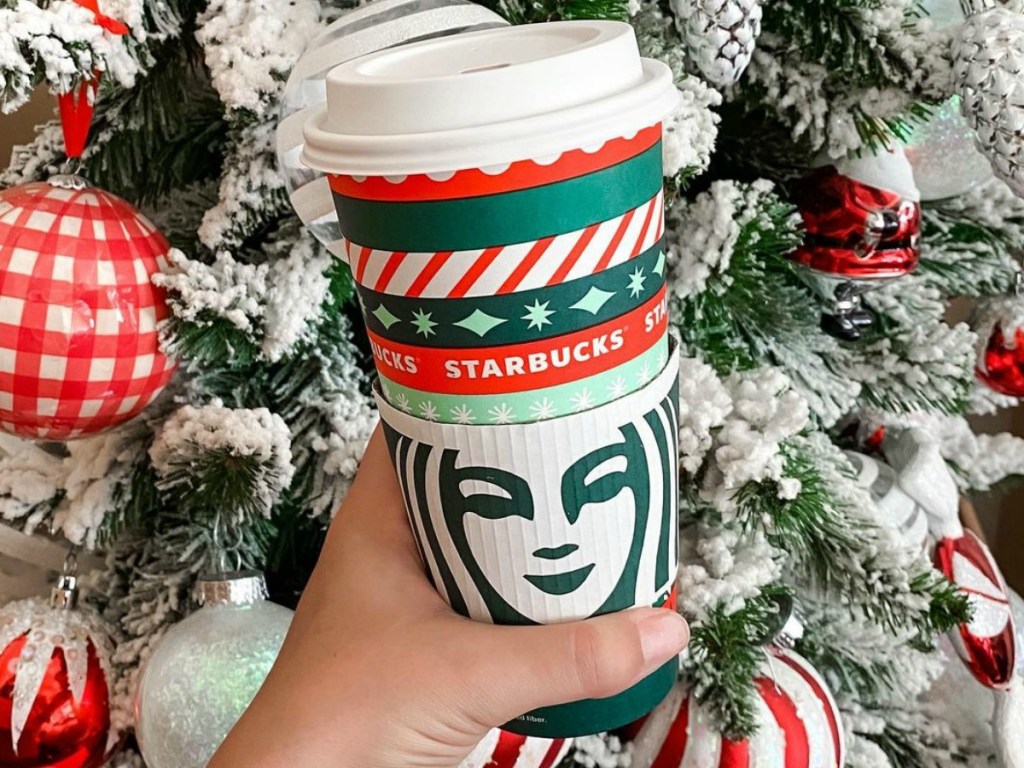person holding Starbucks cup in front of flocked Christmas Tree