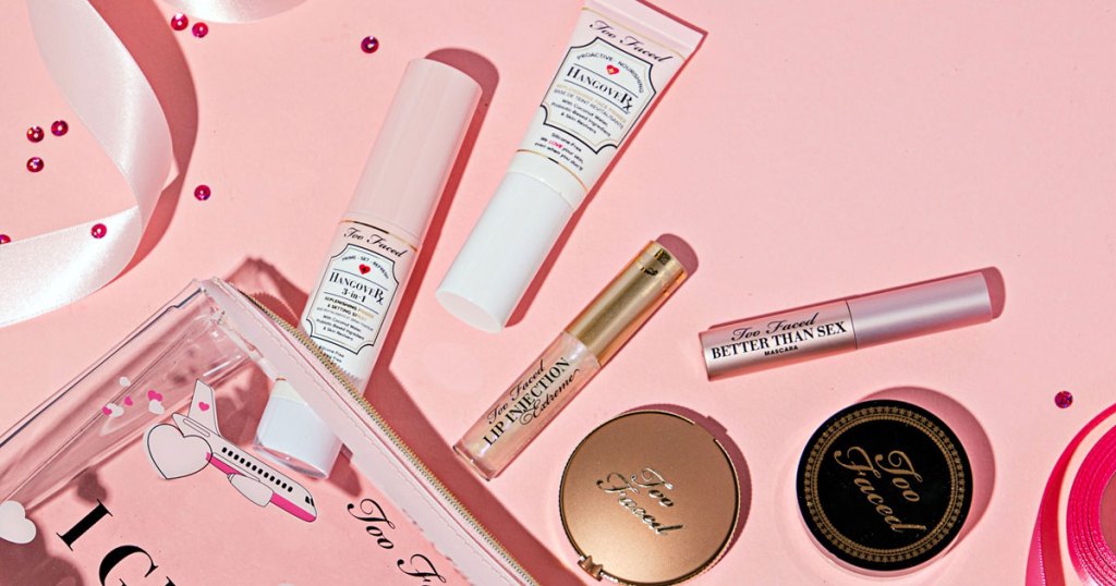 too faced travel size cosmetics coming out of a makeup bag on a pink background