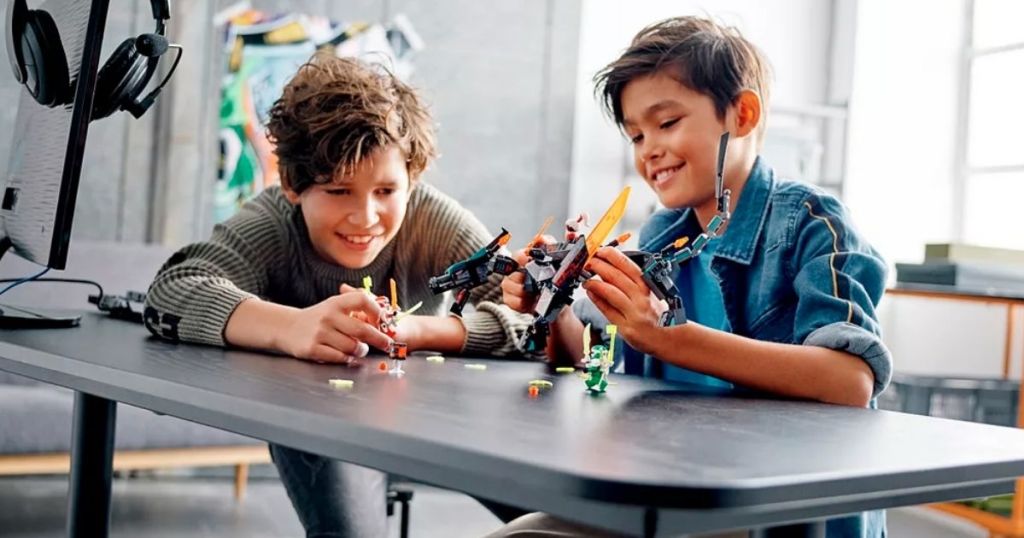 two boys sitting at a table playing with a lego ninjago set