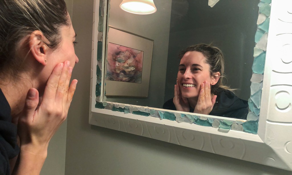 woman in mirror using skincare products