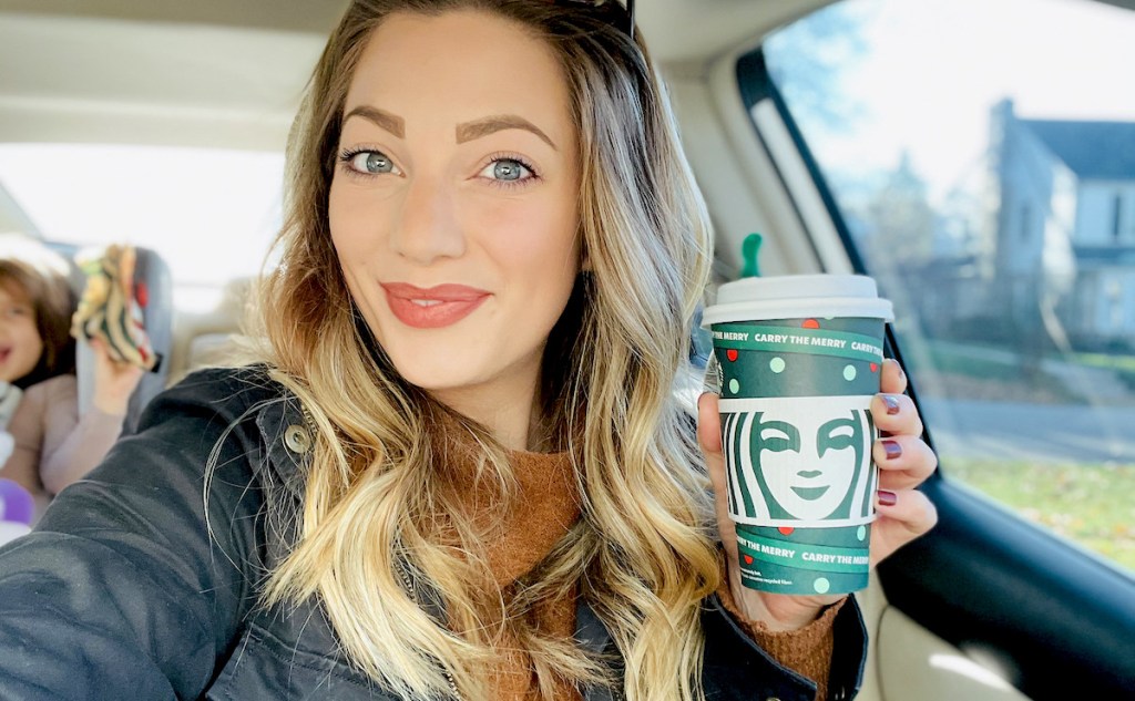 woman holding holiday starbucks cup in car