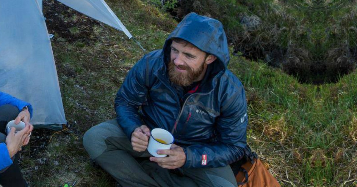 man wearing a columbia rain jacket outside in the rain by a tent