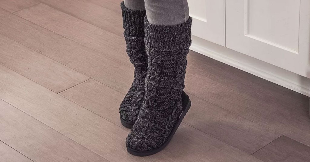 woman standing on hardwood floor wearing a pair of black knit muk luks sweater boots