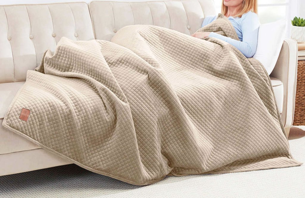 woman sitting on a couch with a tan weighted blanket over her