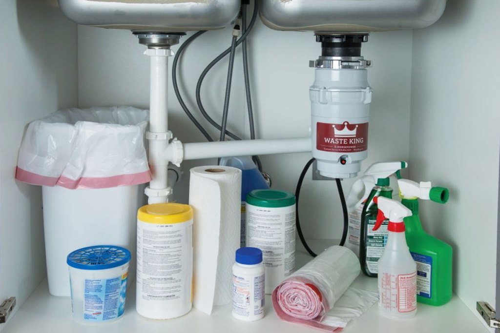 waste king garbage disposal installed under sink with garbage can and cleaning products stored around it