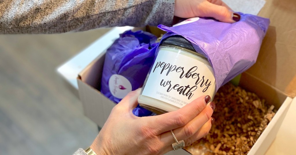 hand pulling out jar candle from purple tissue paper