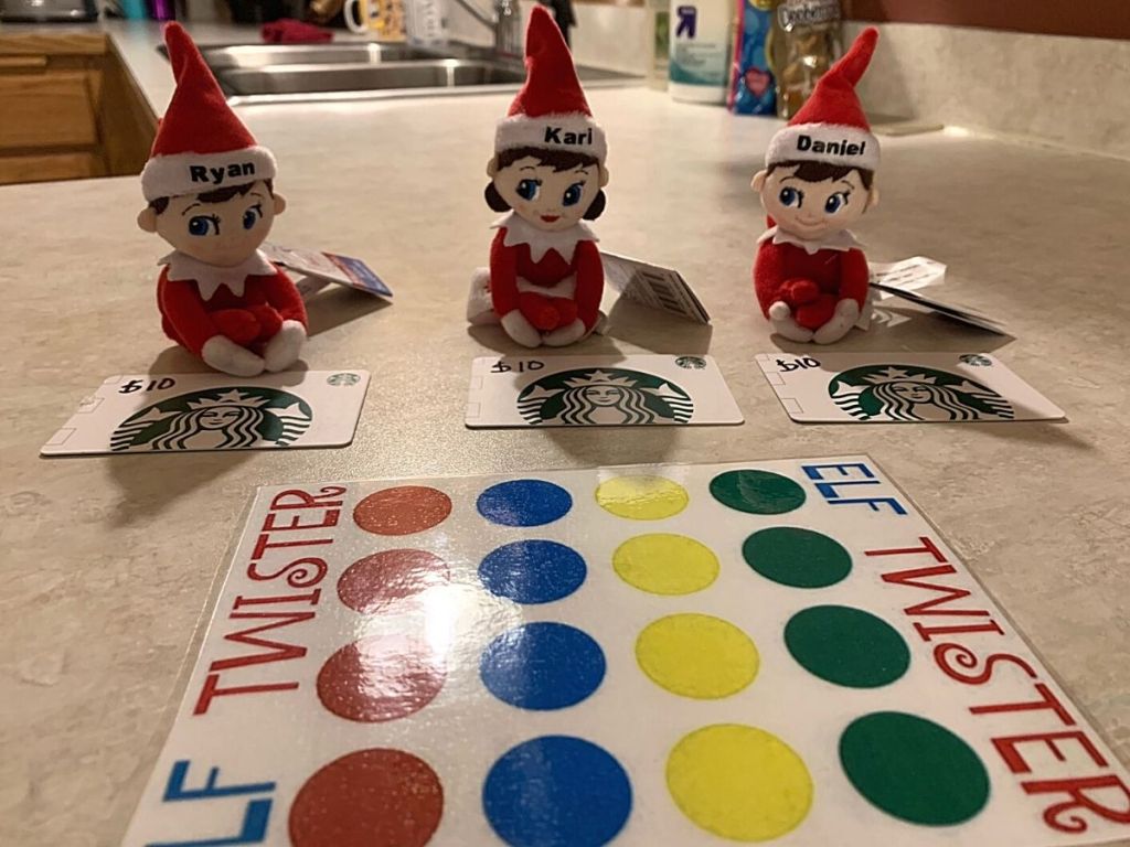 three elves in front of Starbucks gift cards sitting by Elf twister game