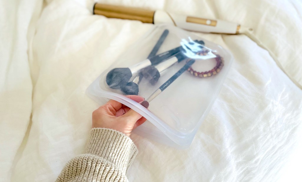 hand pulling makeup brush out of clear bag on bed