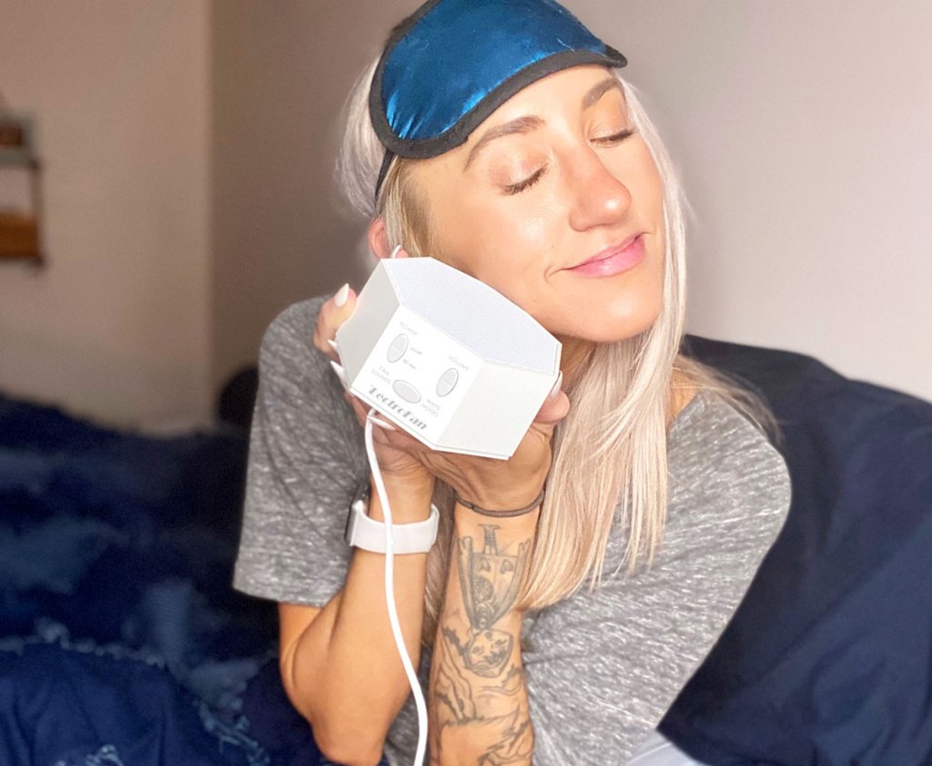 woman sitting in bed with eye mask holding a white noise machine