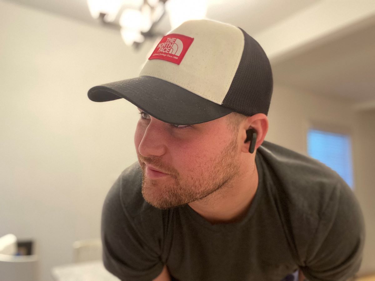 man wearing a hat and earbuds leaning towards the camera