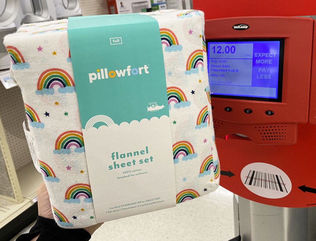 person holding up a set of rainbow print pillowfort flannel sheets next to a red target price scanner