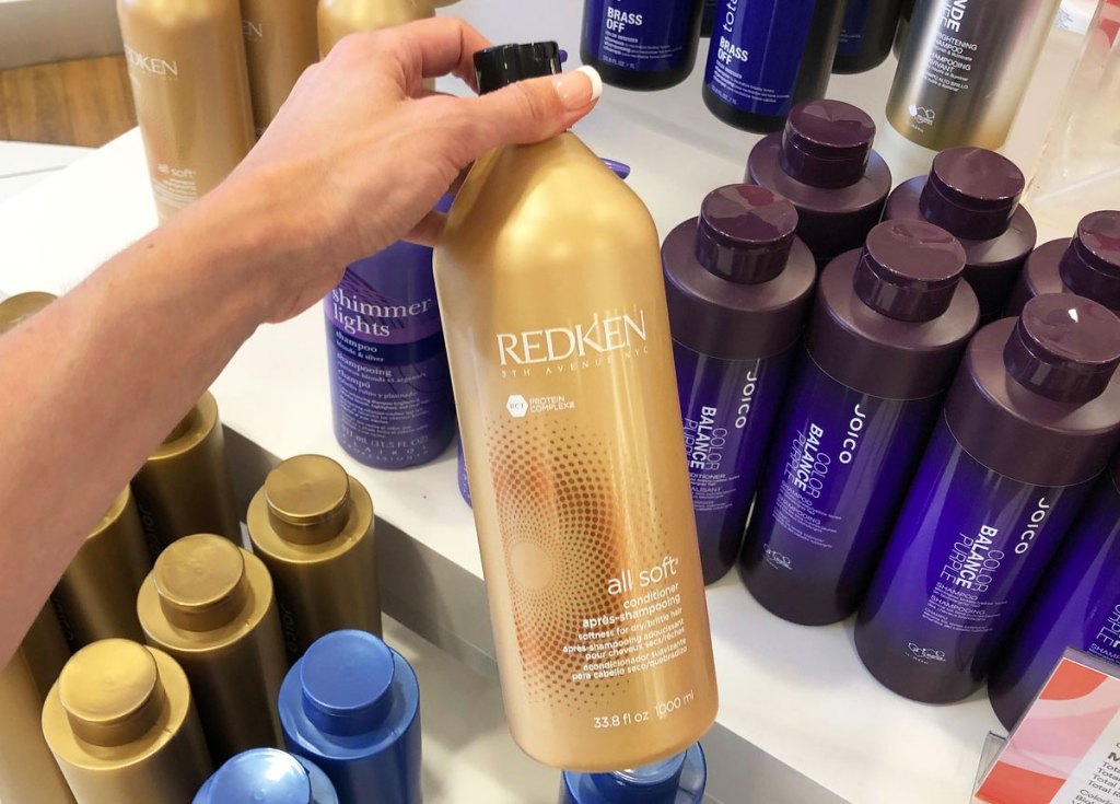 person holding up gold bottle of redken conditioner