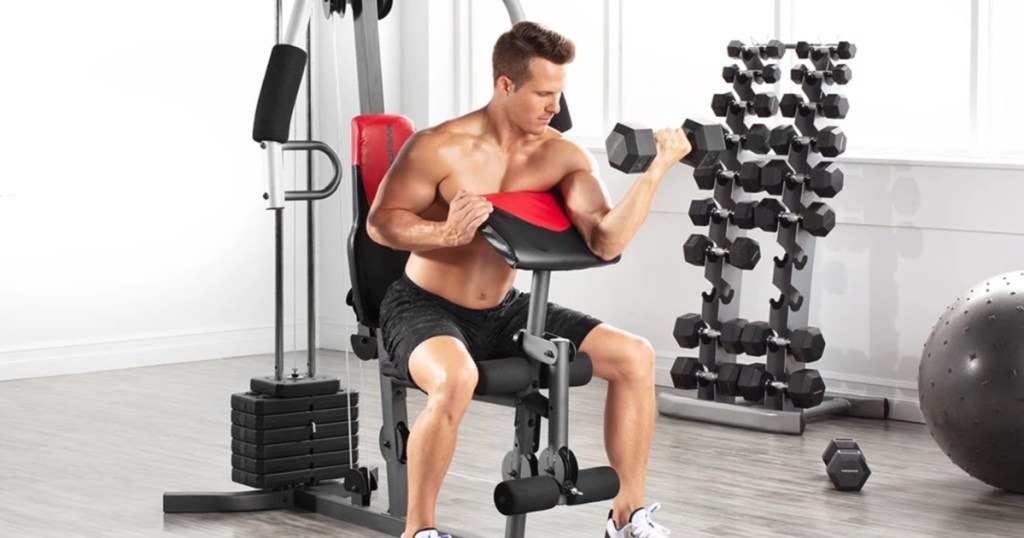 man sitting on a workout bench at home lifting weights