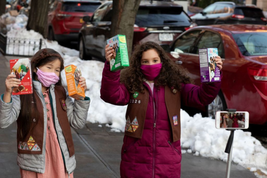 masked Girl Scouts holding boxes of cookies