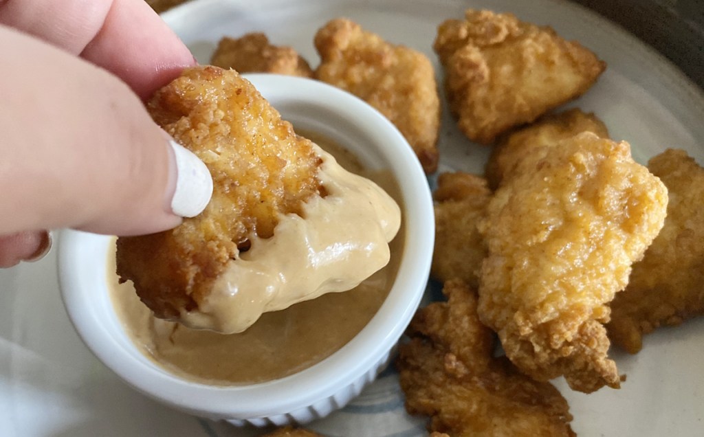 hand dipping chicken in to sauce