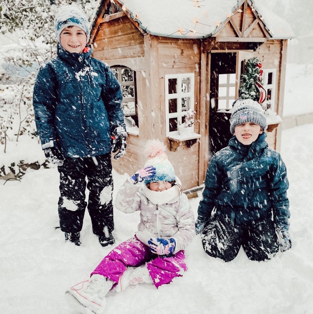 kids in front of playhouse with snow and wearing winter gear