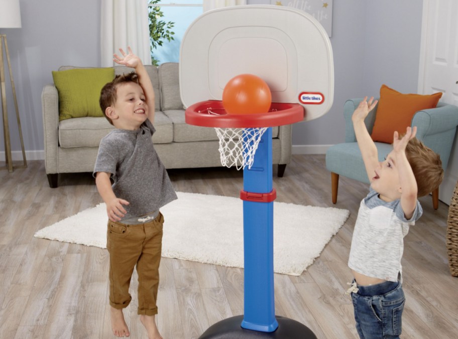 two kids playing on little tikes basketball hoop in living room
