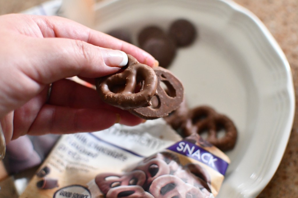 holding 2 chocolate covered pretzels