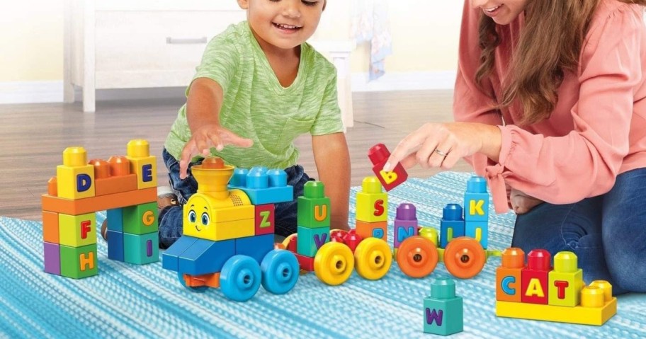 small child and woman sitting on the floor playing with a mega bloks train set