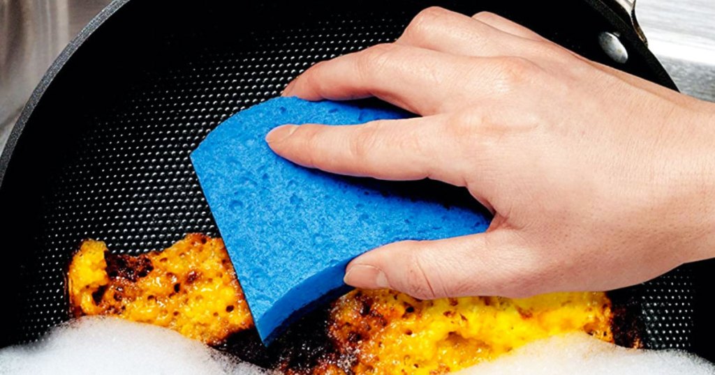 person using a blue sponge on a frying pan