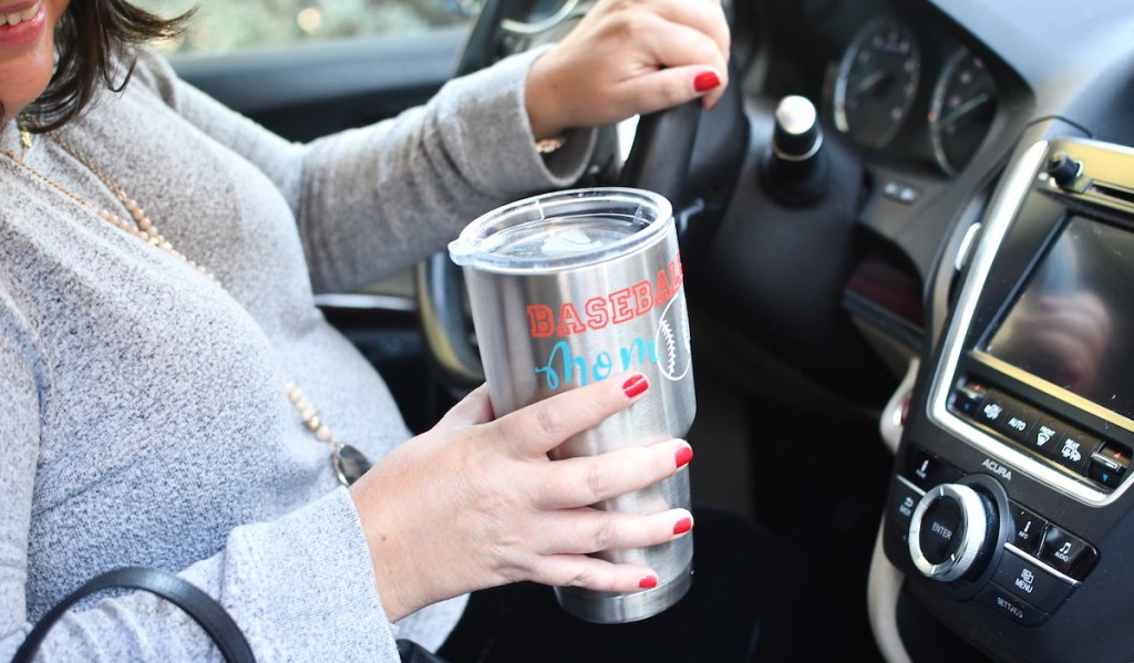 woman sitting in car holding travel coffee mug