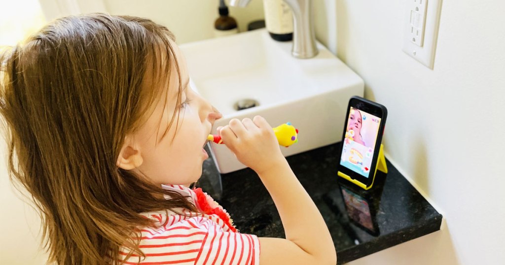 girl brushing her teeth while looking at a phone