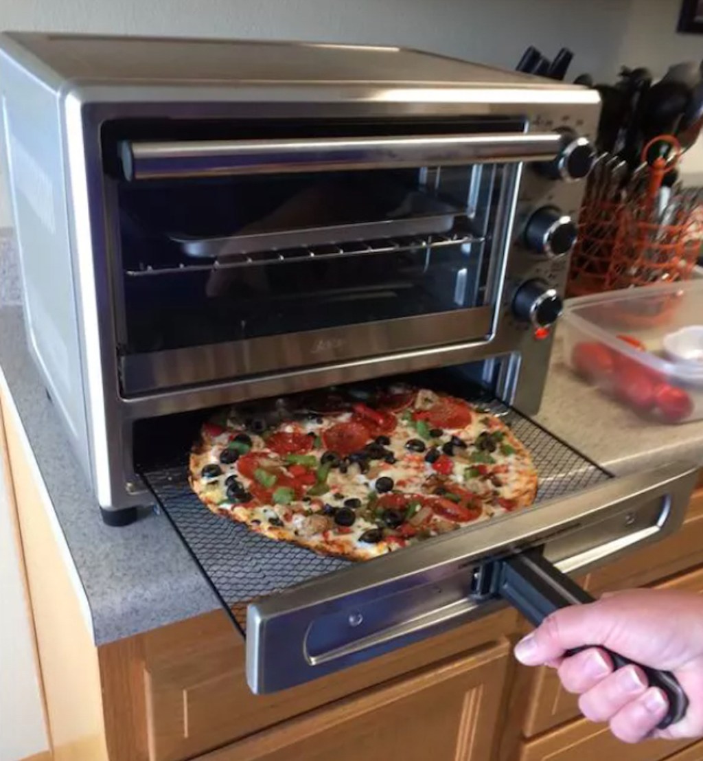 hand pulling out pizza from oster toaster oven drawer