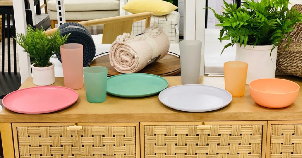 pink plate and cup, green plate and cup, gray plate and cup, and orange plate and cup on dresser in store