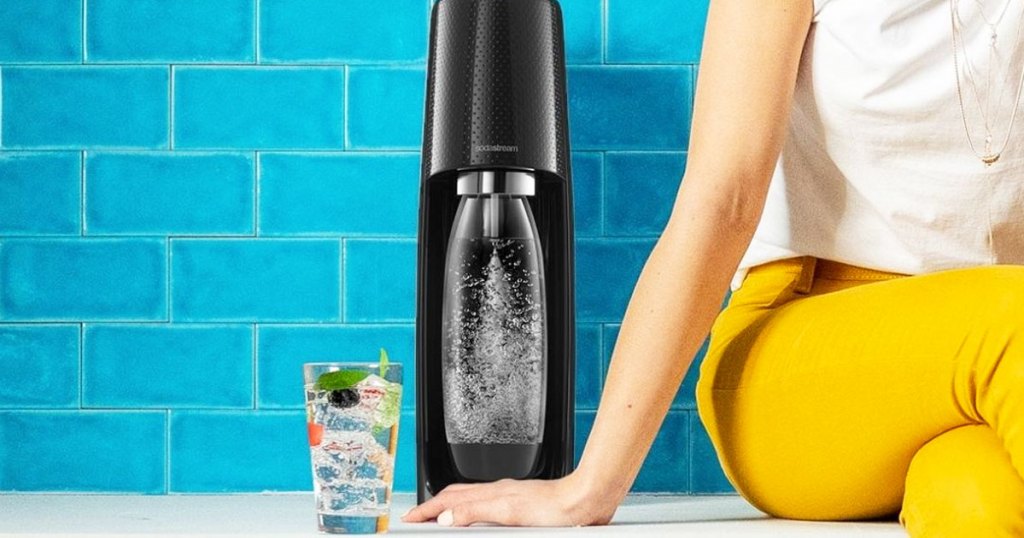 woman sitting on counter next to black sodastream machine making sparkling water