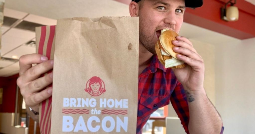 man holding a Wendy's bag and eating a sandwich