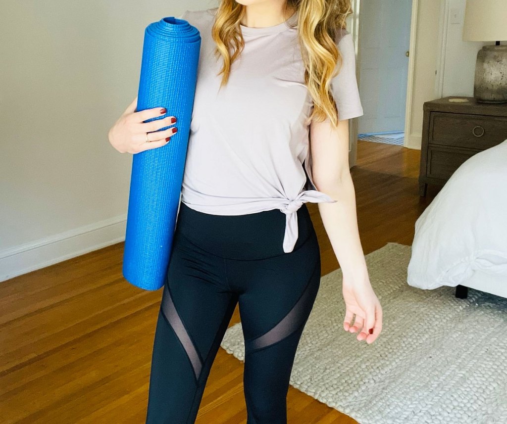 woman in black leggings and pastel top holding a blue yoga mat