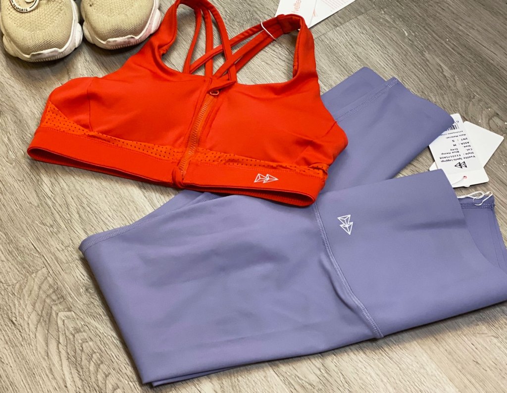 orange sports bra and purple leggings on floor next to running shoes