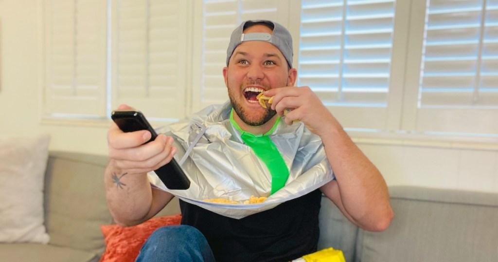 man eating chips holding remote and wearing large bib 