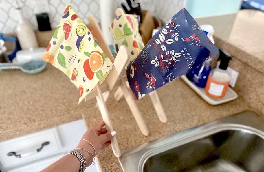 hand holding edge of wooden drying rack with bee's wraps on top