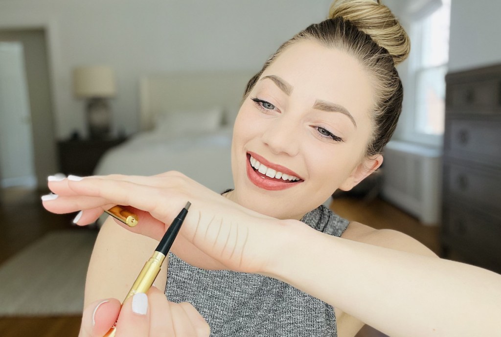 woman holding unibrow universal eyebrow pencil up to hand drawing lines