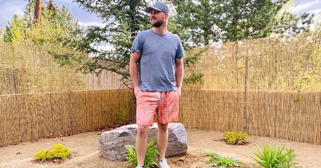 man standing outside wearing gray tee and orange and white shorts
