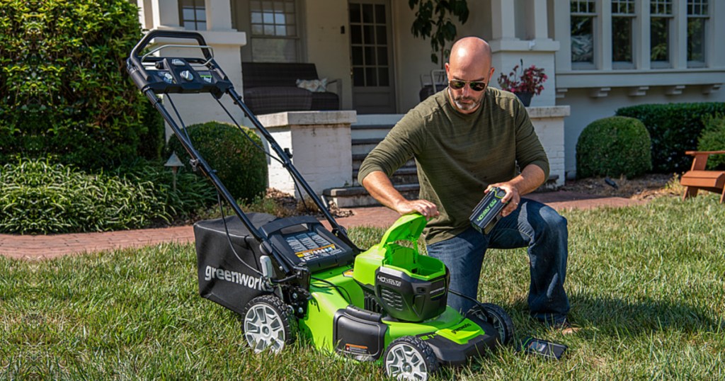 man kneeling next to a greenworks lawn mower