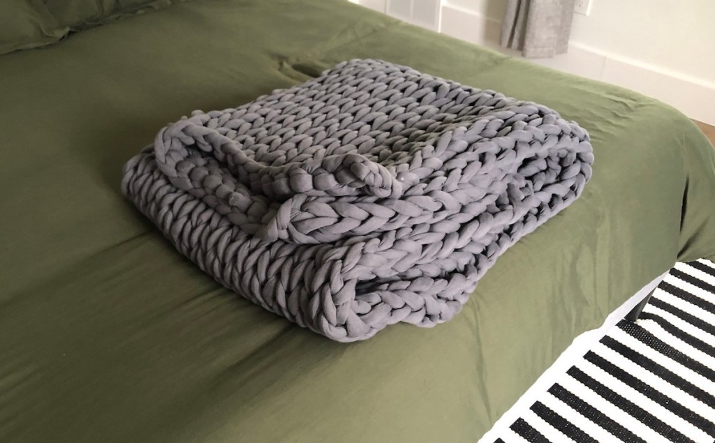 folded gray weighted chunky knit blanket on edge of green bed