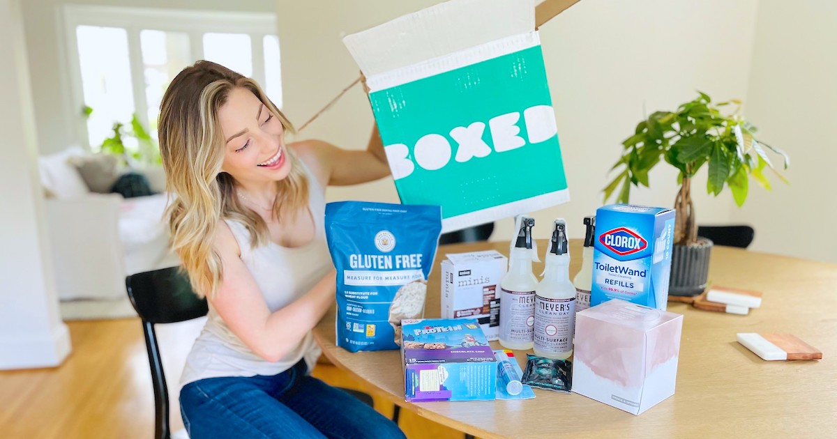 woman sitting at dining room table holding blue boxed box looking at grocery products using boxed promo code