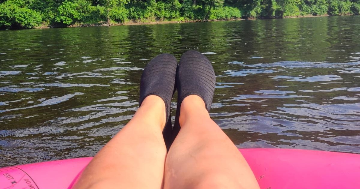 legs wearing black water shoes on pink innertube