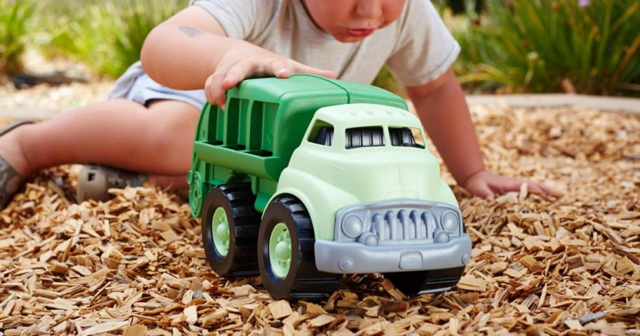 young boy playing with a green plastic garbage truck