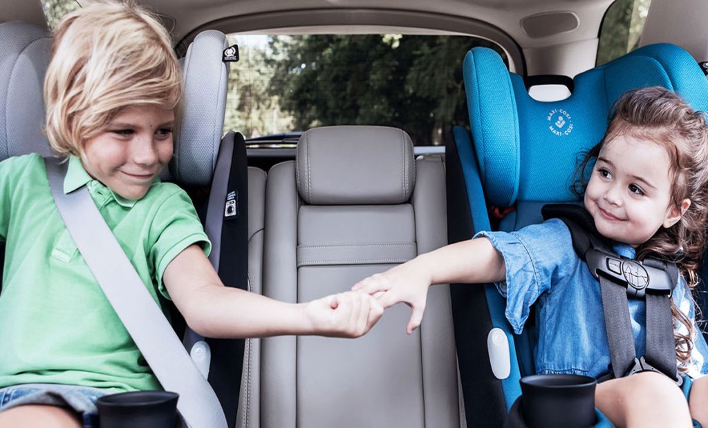 two kids holding hands sitting in car seats in car