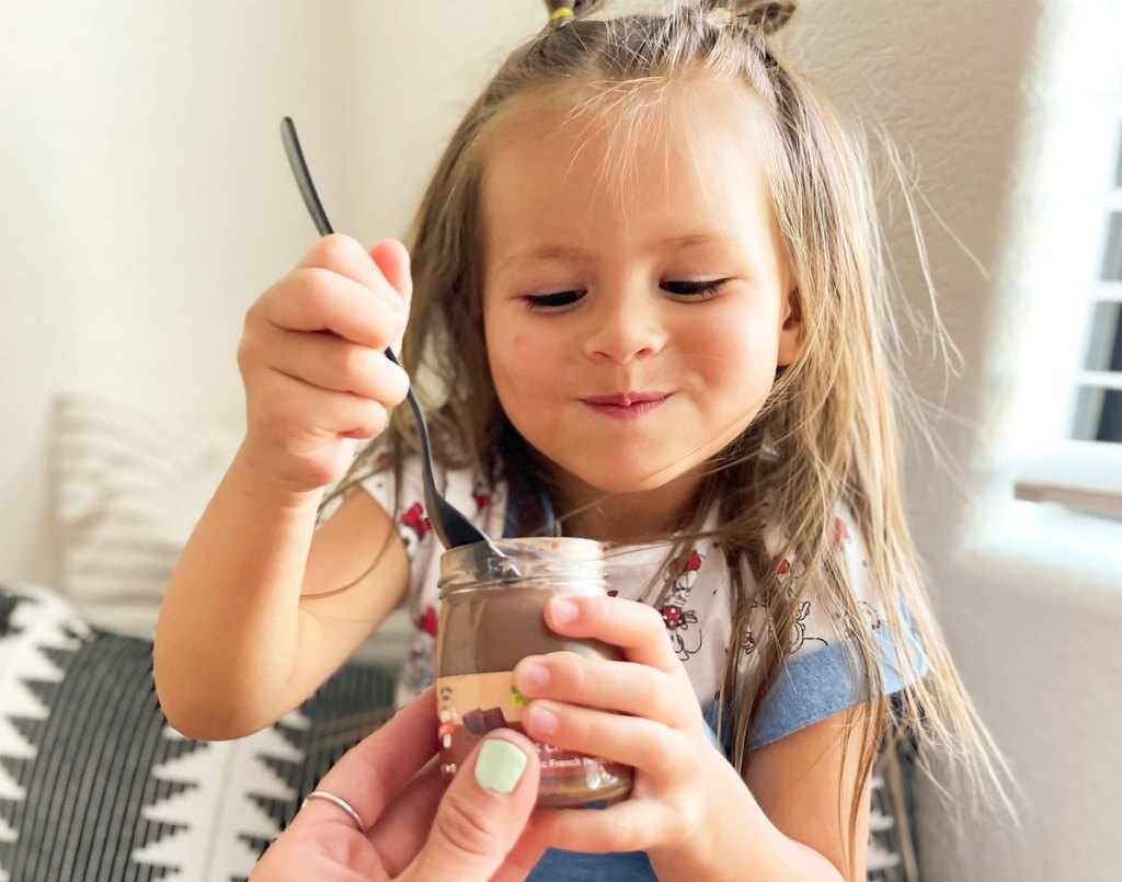 little girl taking spoonful of chocolate pudding