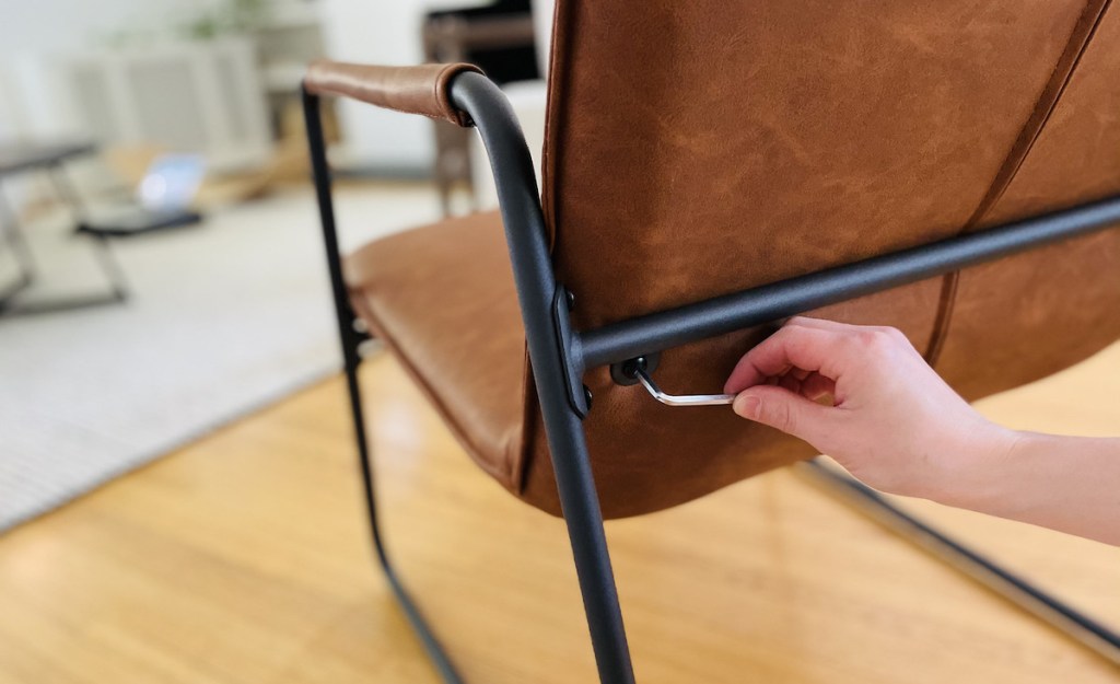 hand screwing bolt into back of brown leather modern chair