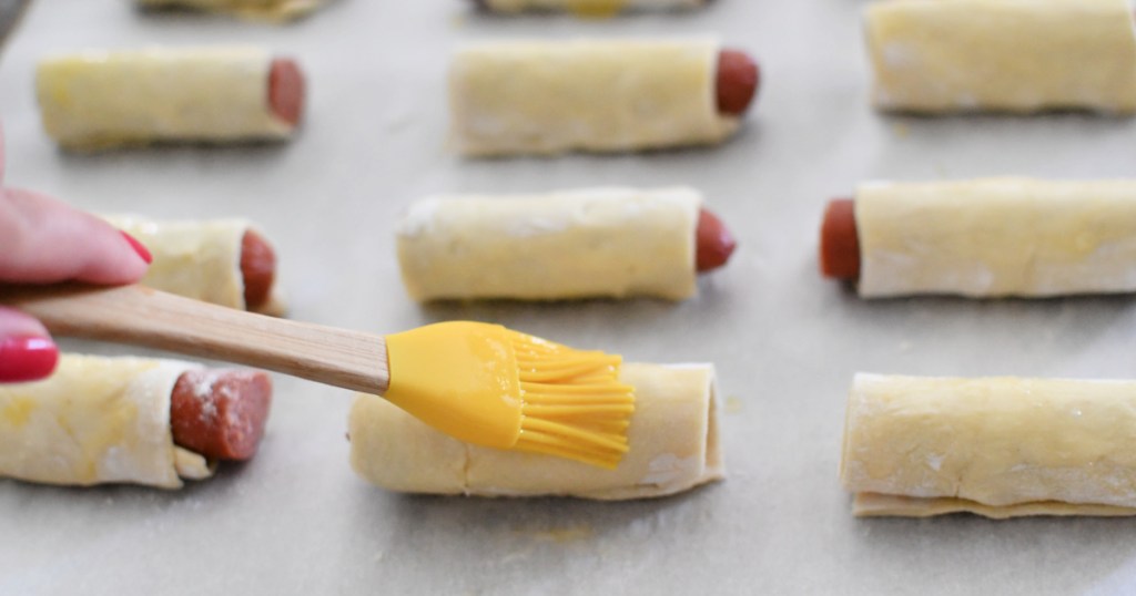 brushing egg wash on pigs in a blanket